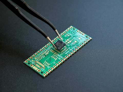 Photo of a forcep holding a microprocessor over a pcb with the intention of soldering them together
